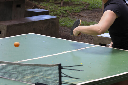 Woman playing an outdoor game of table tennis with concentration. This active sport involves hitting an orange ball over net with small paddle for fun recreation - Powered by Adobe