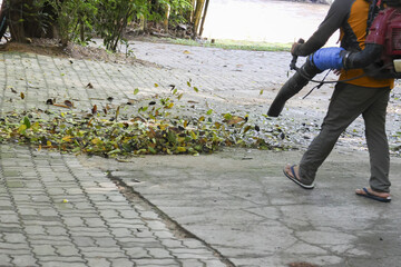 Diligent worker in action cleaning paved sidewalk with an air blower machine. Outdoor maintenance blowing away dry autumn leaf for garden sanitation and general yard work