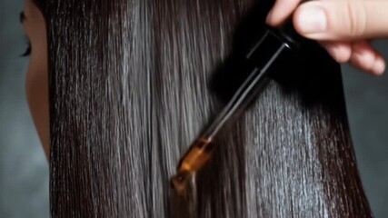 Person applying oil serum to dark, straight hair