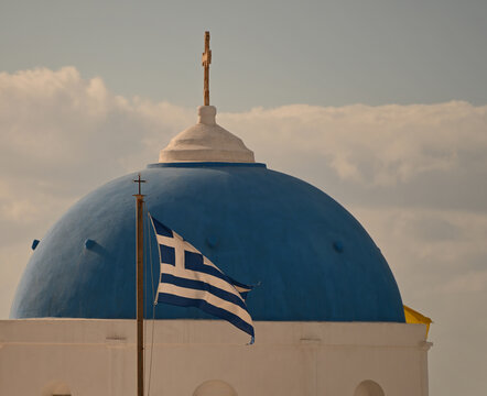 The national flag of Greece flying in front of a blue church steeple.