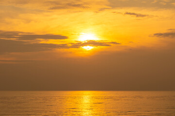 Fototapeta premium Nature sky breathtaking golden sunset over a calm ocean, with the entire sky and water bathed in brilliant shades of yellow and orange. Streaky clouds enhance the dramatic display of light 
