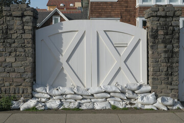 Sandbags stacked in front of a residential gate as flood protection. The image illustrates home safety measures, natural disaster preparedness, and property insurance concerns in coastal or high-risk 