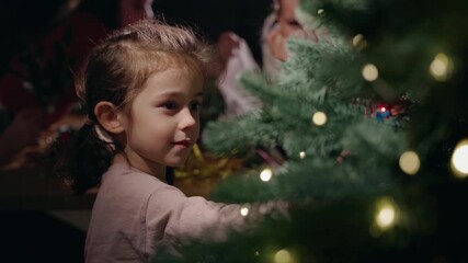A young girl decorates a Christmas tree with glowing lights, surrounded by festive decorations and family members preparing for the holidays at home - Powered by Adobe