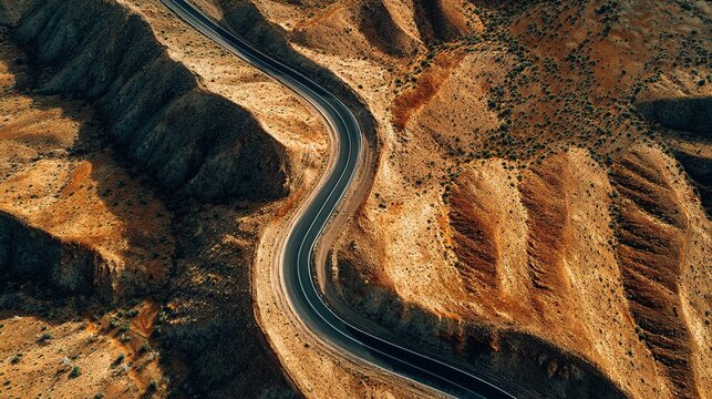 Aerial view of winding asphalt road snaking through dry desert canyon and arid brown hills.