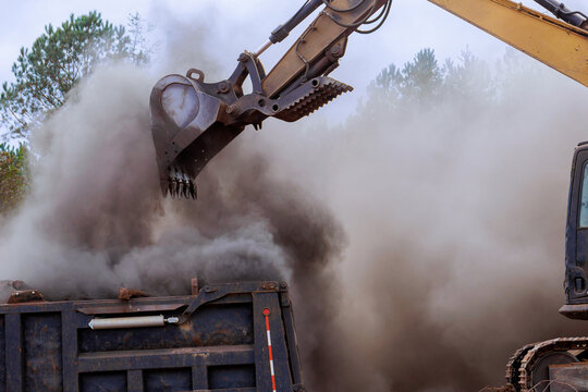 Fototapeta Excavator is lifting dirt debris from ground into dump truck, creating dusty cloud