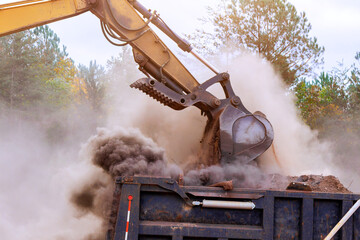 Digger lifts soil from ground into truck, creating clouds of dust in an active construction area. © ungvar