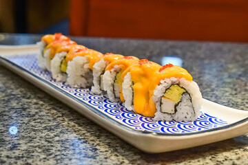 Delicious sushi rolls with spicy sauce and fresh ingredients at a local Asian restaurant. Close up view. mentai. long plate. japanese, japan. blue, white. seaweed.