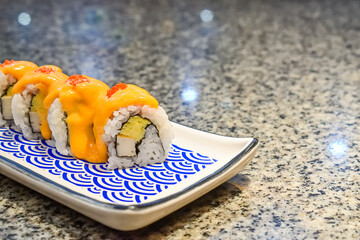 Delicious sushi rolls with spicy sauce and fresh ingredients at a local Asian restaurant. Close up view. mentai. long plate. japanese, japan. blue, white. seaweed. copy space, empty, free, negative.
