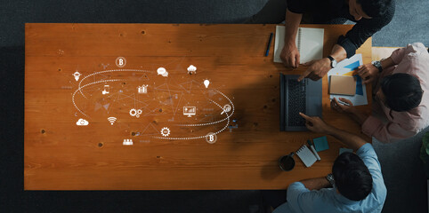 Top view of a collaborative workspace featuring diverse individuals engaged in discussions about digital technology, innovation, and creative ideas on a wooden table. Trope