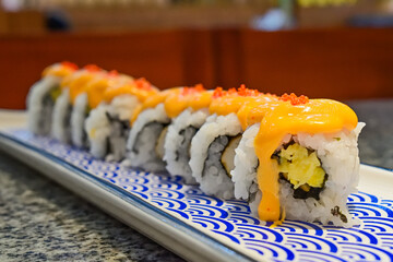 Delicious sushi rolls with spicy sauce and fresh ingredients at a local Asian restaurant. Close up view. mentai. long plate. japanese, japan. blue, white. seaweed.