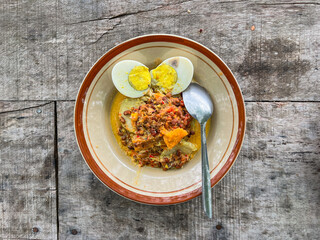 Top view of Lontong Opor Ayam on the plate. Indonesian traditional food, made from chicken cooked with coconut milk and spices. Popular during Eid al Fitr. wooden table. spoon. stainless steel.