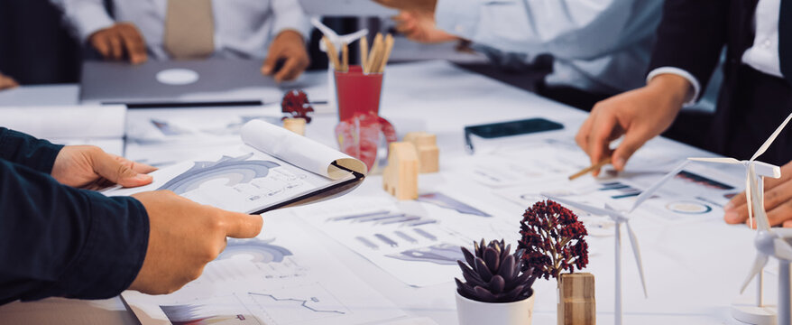 A diverse business team engaged in a collaborative meeting, analyzing environmental charts and graphs to develop sustainable strategies in a modern office setting. SACTR