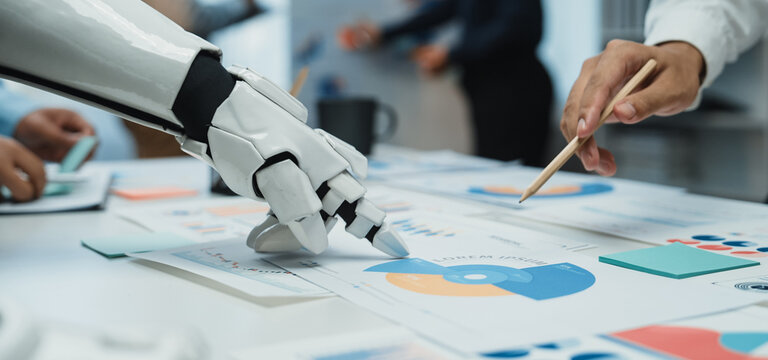 A futuristic scene of a robotic hand assisting a human in analyzing colorful charts and graphs on a table, representing the collaboration between technology and human effort.Noogenesis