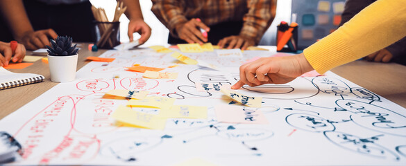 A diverse team gathers around a large paper, engaging in a vibrant brainstorming session using...