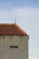 Architectural abstract of a building corner with a red terracotta tiled roof, concrete wall, and small glass block window