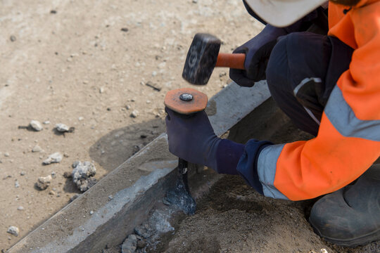 Close-up of builder breaking away concrete using chisel and hammer on construction site