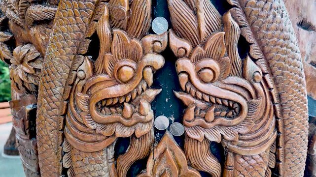 Intricate Thai wood carving of naga dragons on a carved pillar, traditional temple decor and craftsmanship.