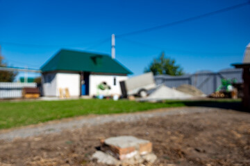 Rural construction site under clear blue sky featuring white house green roof sand piles and building materials