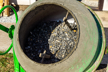 Close-up view inside green concrete mixer drum showing layer of crushed stone ready for mixing