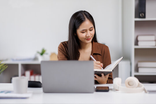 Smiling woman student hand taking notes on notebook and laptop wooden table at home office
