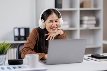 Smiling woman takes notes at her office, wearing headphones listening music at work using laptop remote work. Online education concept
