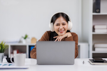 Smiling woman takes notes at her office, wearing headphones listening music at work using laptop remote work. Online education concept
