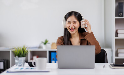 Smiling woman takes notes at her office, wearing headphones listening music at work using laptop remote work. Online education concept
