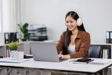 Smiling woman takes notes at her office, wearing headphones listening music at work using laptop remote work. Online education concept
