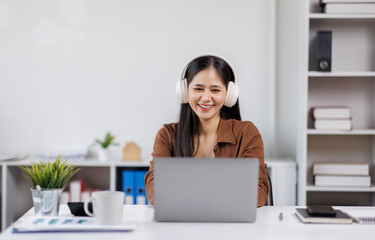 Smiling woman takes notes at her office, wearing headphones listening music at work using laptop remote work. Online education concept
