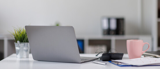 Laptop Computer, notebook, and eyeglasses sitting on a desk in a large open plan office space after working hours	