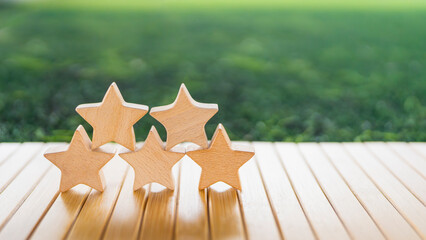 Stacked five wooden stars on table with green background symbolizing high rating, excellent review,...