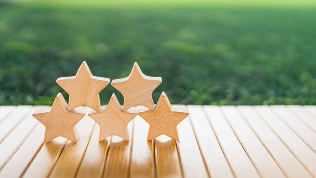 Stacked five wooden stars on table with green background symbolizing high rating, excellent review, top quality, trust, performance ranking, brand credibility, and customer satisfaction.