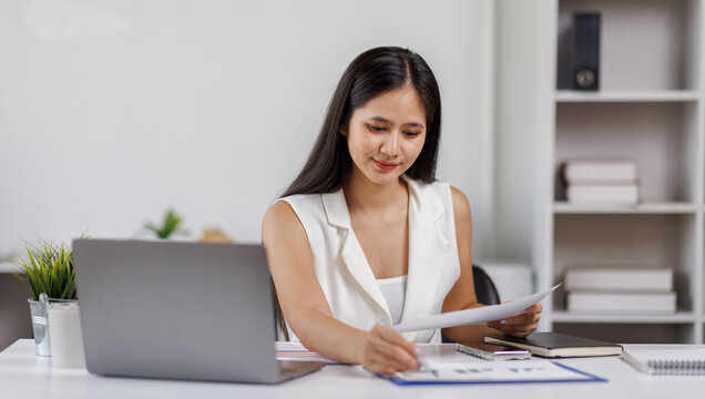 Asian female Using laptop computer and working at office with calculator document on desk, doing planning analyzing the financial report, business plan investment, finance analysis concept.