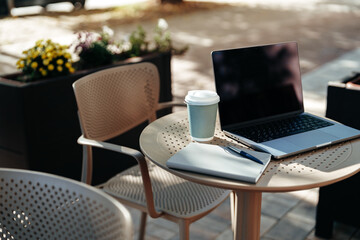 Coffee and laptop on a table in an outdoor cafe setting during a sunny day