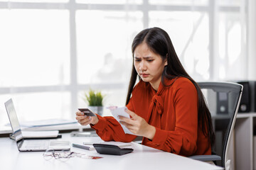 Young asian woman looking at credit card with bill invoice in her hands and worry about cash on bills payday, Business financial concept, 
