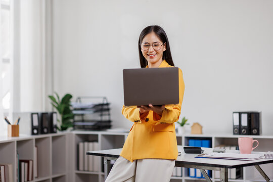 Image of business asian secretary woman standing and holding laptop computer while working in the office
