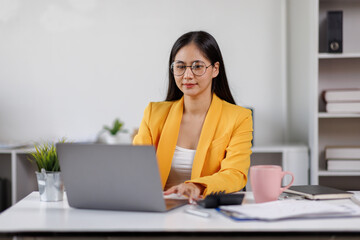 Asian woman smiles while working on her laptop at a bright, modern office desk. happy businesswoman with his work in the office.
