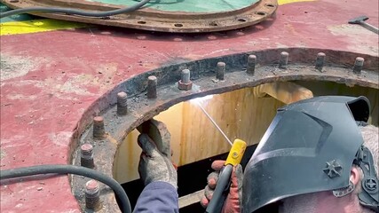 Ship welder repairs and welds a new stud inside wing tank during vessel maintenance operations. shipboard operations, marine industry, maintenance engineering, metal welding, mechanical work