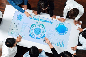 A diverse team collaborates around an interactive table displaying data visualizations for global business strategy, enhancing teamwork and innovation in a modern office setting. Trope