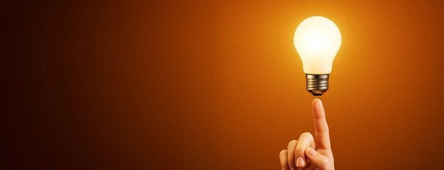 Creative concept with human finger balancing glowing light bulb on orange background symbolizing business innovation and design inspiration template.