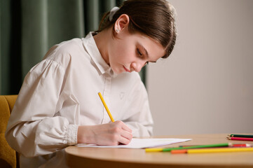Girl diligently completes homework. Young girl focuses on schoolwork while drawing with colored pencils. Hobbies, development and learning, children's creativity, imagination, fine motor skills.