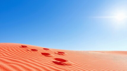 Footprints lead across undulating, vibrant red sand dunes under a bright, clear blue sky, suggesting a journey or exploration.