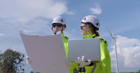Female engineer holding laptop discussing data with colleague near wind turbine analyzing renewable energy project teamwork concept of professional innovation sustainable power environment - Powered by Adobe