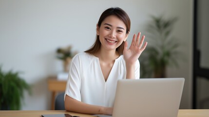 Professional woman smiling and waving at laptop in modern office environment showcasing success, communication, technology, and confidence in a corporate setting