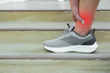 Runner clutching painful ankle on wooden stairs, highlighting sports injury. Outdoor rehab concept...