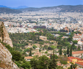 Fototapeta premium View of the Temple of Hephaestus and the Ancient Agora surrounded by greenery, with the modern Athens cityscape in the background