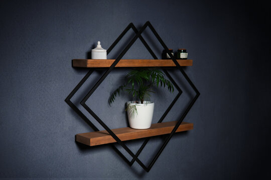Modern wall shelf with geometric design. Decorative wooden and metal shelf on a dark wall. Designer diamond-shaped wall shelf in loft style