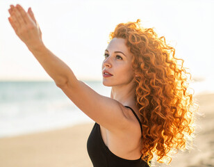 Woman with red curly hair reaches towards the sun on a sunny beach