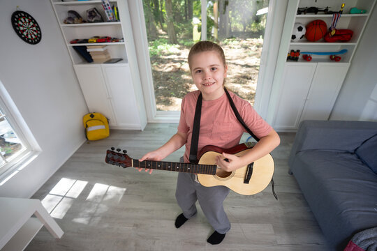 Child playing guitar. Teenager practicing guitar music in living room. Kid learning guitar indoors. Boy with guitars during music lesson. Kid playing acoustic guitar. Child practicing songs.