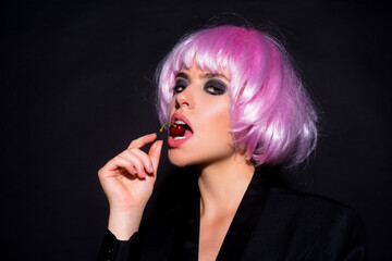 Cherry in sensual woman mouth, sensual look. Beauty model with with pink wig and sexy makeup. Glamorous fashion concept. Sensual girl character with lick cherry. Sensual beauty and taste.
